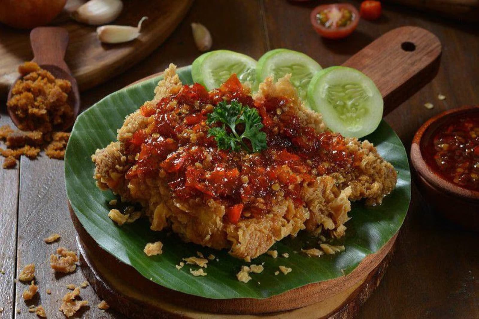 Chicken geprek topped with sambal and served with cucumber.